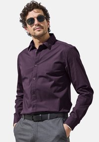Dark purple button-up shirt with a collar and long sleeves, paired with gray patterned trousers and a black belt; model wears sunglasses.