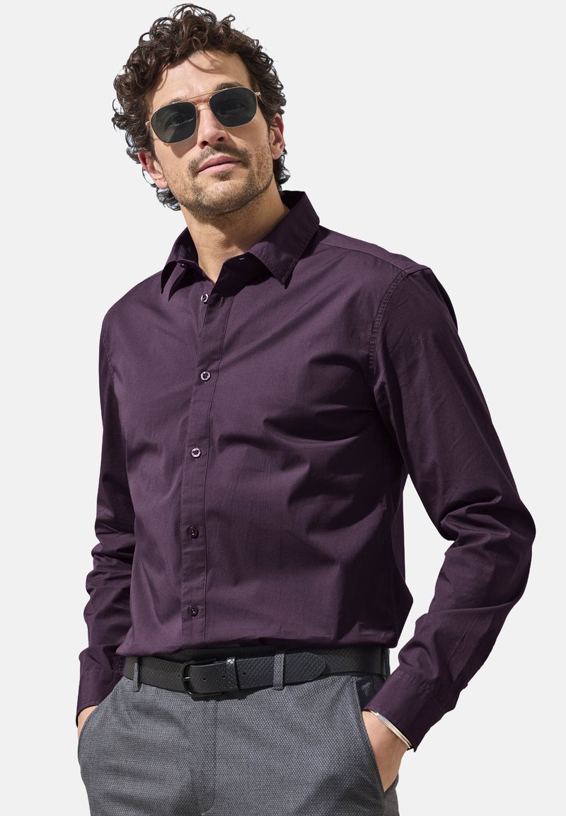 Dark purple button-up shirt with a collar and long sleeves, paired with gray patterned trousers and a black belt; model wears sunglasses.