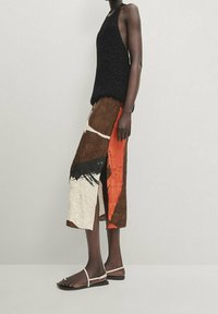 Top in maglia nera abbinato a una gonna patchwork lunga fino al ginocchio, caratterizzata da colori marroni, crema e arancioni, con una texture sgualcita e uno spacco laterale.