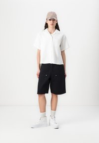 White short-sleeve button-up shirt, black denim shorts, beige cap, paired with white high-top sneakers and grey socks. Simple design and clean lines.