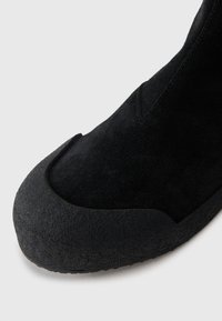 Bottines chelsea en suede noir avec un embout arrondi en caoutchouc texturé et un talon en cuir lisse. Présentent un design ajusté et des détails de couture minimalistes.