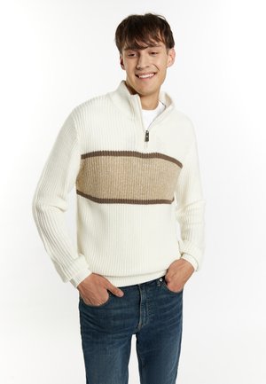 Witte gebreide trui met een half-rits kraag, met een horizontaal beige gestreept patroon. Gecombineerd met blauwe jeans. Zachte textuur.