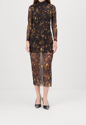 Femme portant une robe midi légère à manches longues avec un motif abstrait brun foncé et orange, associée à des escarpins noirs à bout pointu.
