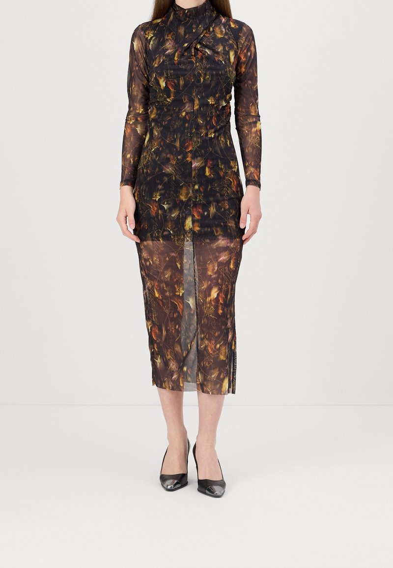 Femme portant une robe midi légère à manches longues avec un motif abstrait brun foncé et orange, associée à des escarpins noirs à bout pointu.