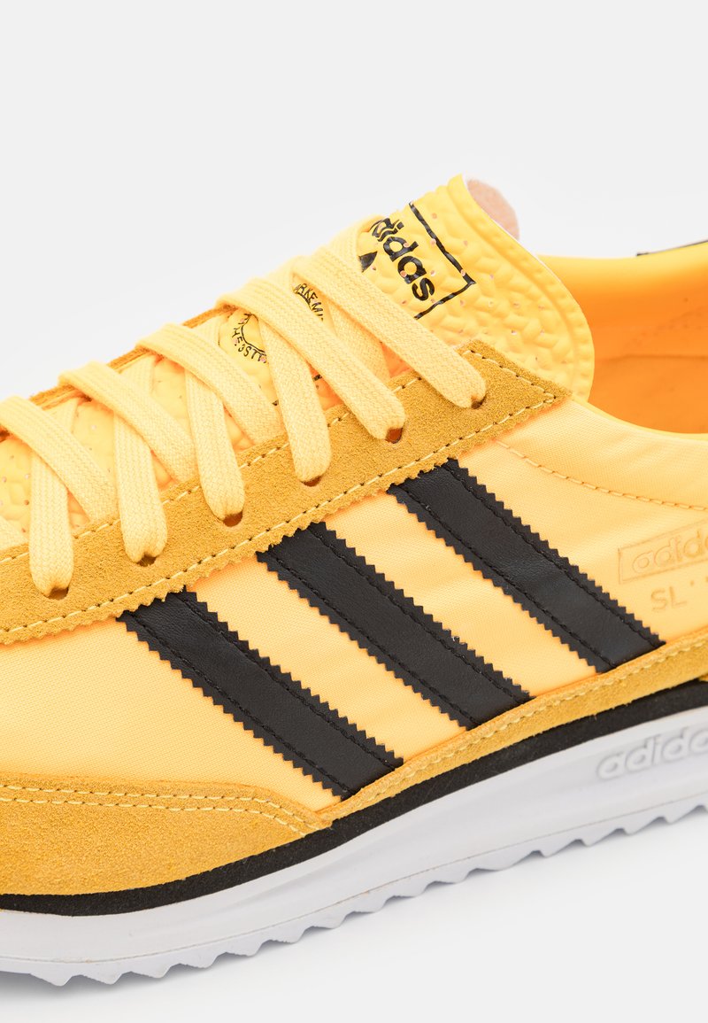 Gelbe Sneaker mit schwarzen Streifen und Schnürsenkeln; aus synthetischem Material und Wildleder; mit einer strukturierten Zunge und einer weißen Gummisohle.