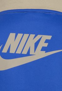 Modra tkanina z gladko teksturo ima poudarjen sivi Nike logotip in obliko swoosh, postavljeno na svetlejši podlagi.