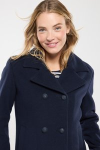 Abrigo de lana mezclada en color navy, con doble botonadura, amplias solapas, dos bolsillos frontales y botones negros. El modelo lleva una camiseta de rayas debajo.