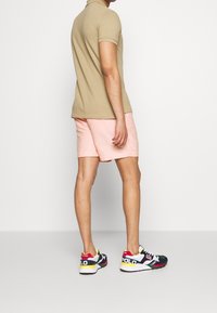 Polo beige, pantaloni corti rosa e sneakers multicolori con dettagli del logo. La vestibilità è casual, con colletto classico e maniche corte.