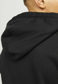Black hooded sweatshirt featuring a soft fabric texture, with visible stitching details at the collar and hood seam.