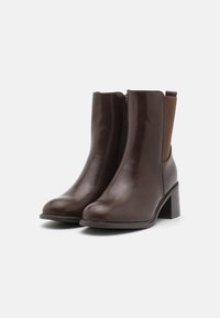 Stivali ankle in pelle marrone con punta arrotondata, zip laterale e tacco a blocco texturizzato. Pannelli elastici laterali in un colore complementare.