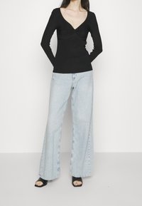 Czarna bluzka z długim rękawem, dekoltem w kształcie litery V i detalem skrętu, połączona z jasnoniebieskimi dżinsami o szerokich nogawkach i czarnymi sandałami na obcasie.