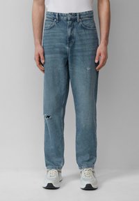 Jasnoniebieskie dżinsy w luźnym kroju, z przetarciem na kolanie, prostymi nogawkami i klasycznym pięciokieszeniowym designem. Noszone z jasnymi trampkami.