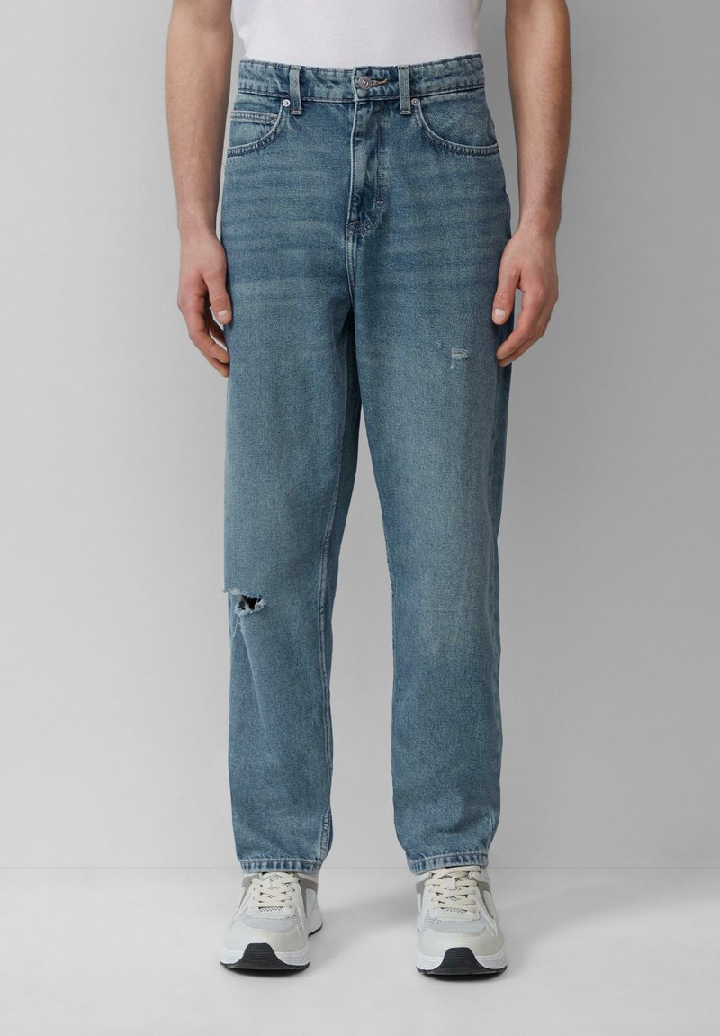 Jasnoniebieskie dżinsy w luźnym kroju, z przetarciem na kolanie, prostymi nogawkami i klasycznym pięciokieszeniowym designem. Noszone z jasnymi trampkami.