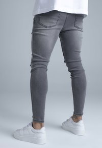 Szürke, stretch farmer skinny nadrág sima textúrával, hátsó zsebekkel, fehér tornacipővel párosítva.