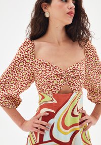 Robe colorée avec un haut à imprimé léopard rouge et vert, des manches bouffantes et une jupe fluide à motifs multicolores.