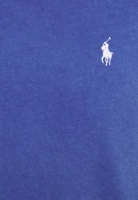 Blå bomulls polo skjorta med ribbad textur, med en vit broderad hästlogotyp på övre vänstra sidan.