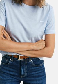 Lichtblauw, kortarm katoenen T-shirt met een ronde hals en een subtiele textuur. Draagt goed in combinatie met donkerblauwe denim jeans en een bruine riem met een zilveren gesp.