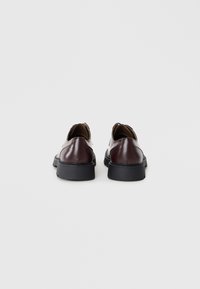 Zapatos de cuero marrón con un acabado suave, punta redondeada y suela de goma negra. Presentan un diseño minimalista y un cosido resistente.