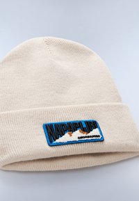 Berretto in maglia beige con risvolto, caratterizzato da una toppa ricamata blu e nera che raffigura montagne e il nome del marchio.