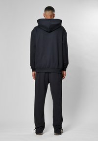 Felpa nera con cappuccio, con orlo e polsini a costine, abbinata a pantaloni coordinati, mostrata da dietro con una finitura liscia e textured.