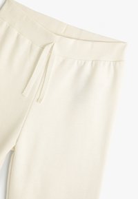 Pantalons de survêtement couleur crème avec une taille côtelée, un cordon de serrage et une texture douce ; conçus pour le confort et une tenue décontractée.