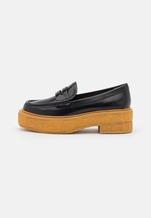 Mocassin noir en cuir avec bride penny et semelle épaisse en crêpe couleur tabac texturée, présenté de profil sur fond clair uni.
