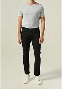 Jeans negros de corte slim, combinados con una camiseta de manga corta gris claro y zapatillas blancas, sobre un fondo neutro.