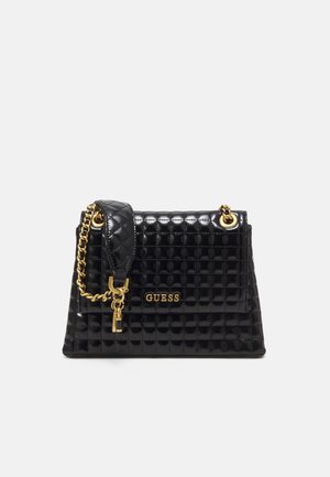 Sac à main noir matelassé avec une finition brillante, accents en métal doré, bandoulière en chaîne et logo "GUESS" affiché en évidence sur le devant.