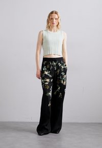 Lys grøn, ribbet crop top parret med sorte bukser med bred ben, der har et blomsterprint i nuancer af grøn og beige.