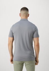 Cămașă polo gri, realizată dintr-un material ușor, având guler clasic și mâneci scurte. Spatele prezintă o textură fină și o cusătură subtilă la margine.