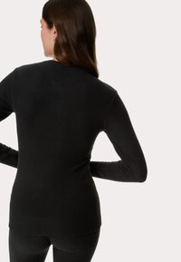 Maglietta nera a maniche lunghe realizzata in un tessuto morbido, design aderente, con scollatura rotonda e costruzione senza cuciture. Adatta per essere indossata a strati.