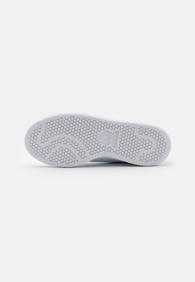 Semelle de sneaker blanche avec un motif texturé hexagonal. Présente un design de vague légèrement surélevé et un logo bien visible. Surface propre et lisse.