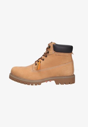 Bottine cheville en daim tan avec col rembourré noir, lacets marron et accent orange. Présente une semelle en caoutchouc texturé avec des crampons profonds pour une meilleure adhérence.