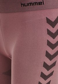Leggings rosa realizzati in tessuto elasticizzato, con vita a coste e motivi a zigzag neri lungo il lato. Logo del marchio in alto.