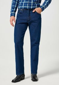 Jeans di jeans blu scuro con taglio dritto e design a cinque tasche. Indossati con una camicia a quadri e stivali neri con tacco.