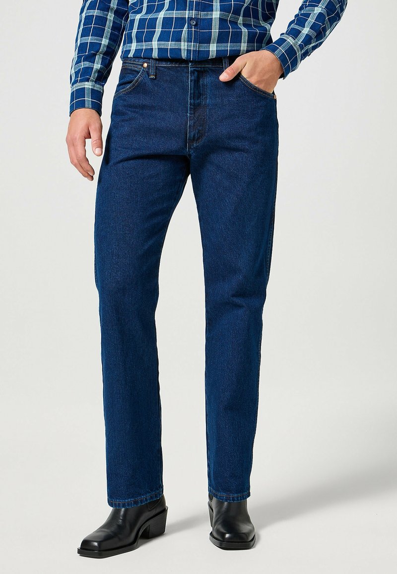 Jeans di jeans blu scuro con taglio dritto e design a cinque tasche. Indossati con una camicia a quadri e stivali neri con tacco.