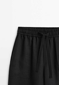 Shorts noirs à taille élastique avec cordon de serrage et grandes poches avant sur fond blanc uni.