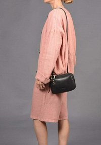 Vestido de lino rosa con mangas largas, detalles de botones y un ajuste relajado; combinado con un pequeño bolso de cuero negro cruzado con detalles en dorado.