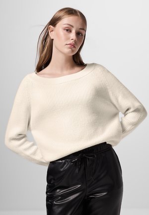 Weißer gerippter Strickpullover mit weitem Ausschnitt und langen Ärmeln, kombiniert mit schwarzen glänzenden Hosen mit Kordelzugbund.