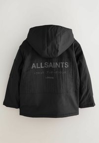 Melnā kapuce jaka ar faktūru aizmugurē, kurā redzams zīmola "ALLSAINTS" logo un cits teksts pelēkā krāsā. Priekšpuse ir gluda.