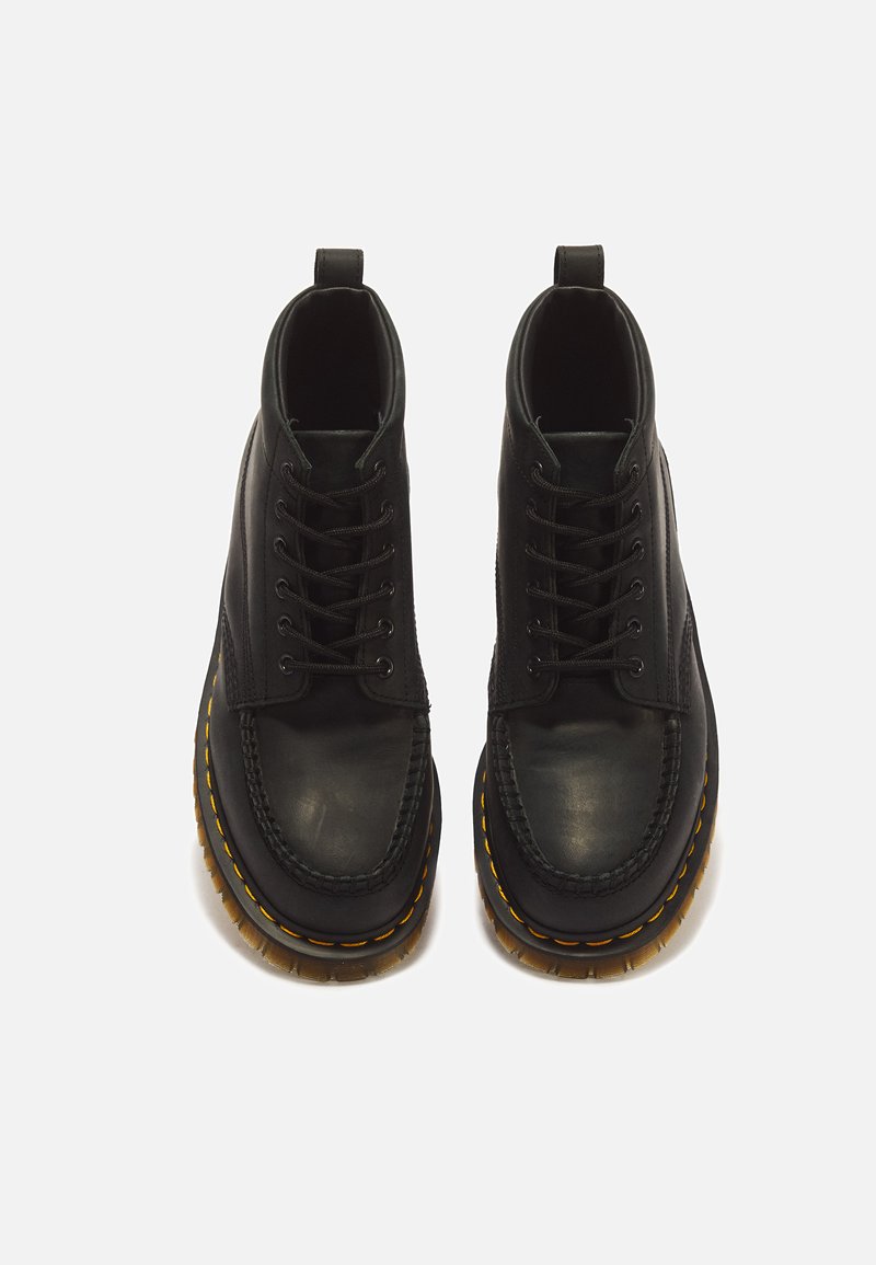 Paar schwarze Leder-Schnürstiefel mit dicken, gelb abgesteppten Sohlen und Zuglaschen hinten auf weißem Hintergrund.