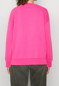 Fleece-tröja i klar rosa med rundad halsringning, nedhasande axlar och ribbade ärmslut. Har en avslappnad passform och en mjuk textur.
