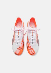 Bílé a oranžové sportovní boty s síťovaným svrškem, černými akcenty a kontrastními tkaničkami. Mají elegantní, aerodynamický design pro maximální výkon.