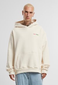 Beige kapucnis felső, pamut keverékből készült, elülső zsebbel és húzózsinórral ellátott kapucnival, kis rózsaszín és zöld feliratos logóval a mellen.