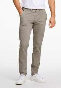 Beige slim-fit broeken met een gestructureerd patroon, met zijzakken en een knoopsluiting, gecombineerd met witte sneakers.