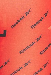 Reebok aktivní oděv v jasně červené barvě s černými logy a akcenty, hladkou texturou a opakujícím se vzorem.