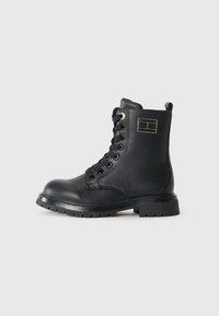 Scarpe stivali alla caviglia in pelle nera con punta tonda, lacci sul davanti, dettagli dorati e suola in gomma. Presentano un logo sul lato e un tallone rinforzato.
