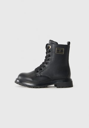 Bottines en cuir noir avec bout rond, lacées à l'avant, accents dorés et semelle en caoutchouc. Présente un logo sur le côté et un talon renforcé.