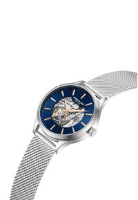 Reloj automático con caja de acero plateado y correa de malla, esfera azul marino con un diseño esqueleto, acentos en oro y plata, y marcadores de hora plateados.
