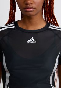 Woman wearing black Adidas sports shirt with white stripes on shoulders and logo on chest, red braided hair visible.